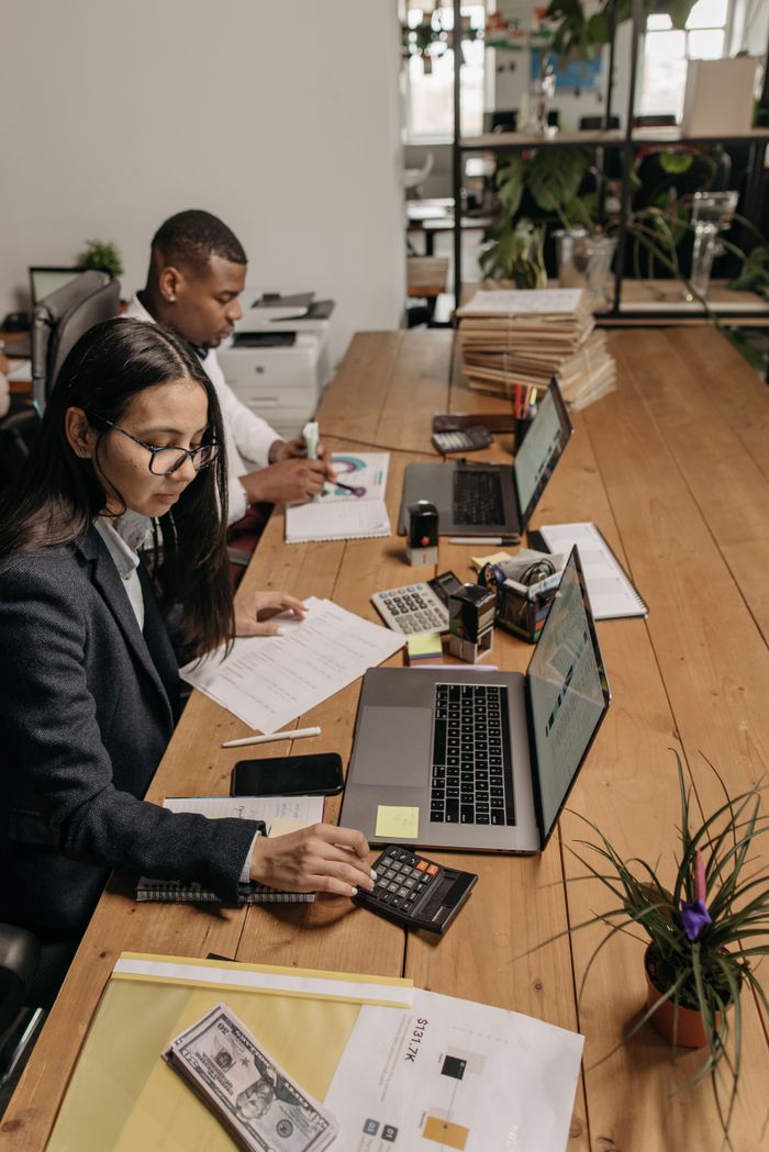 Mastering the First Impression: Your intriguing post title goes here Two diverse accountants working at a shared office table using laptops and calculators.